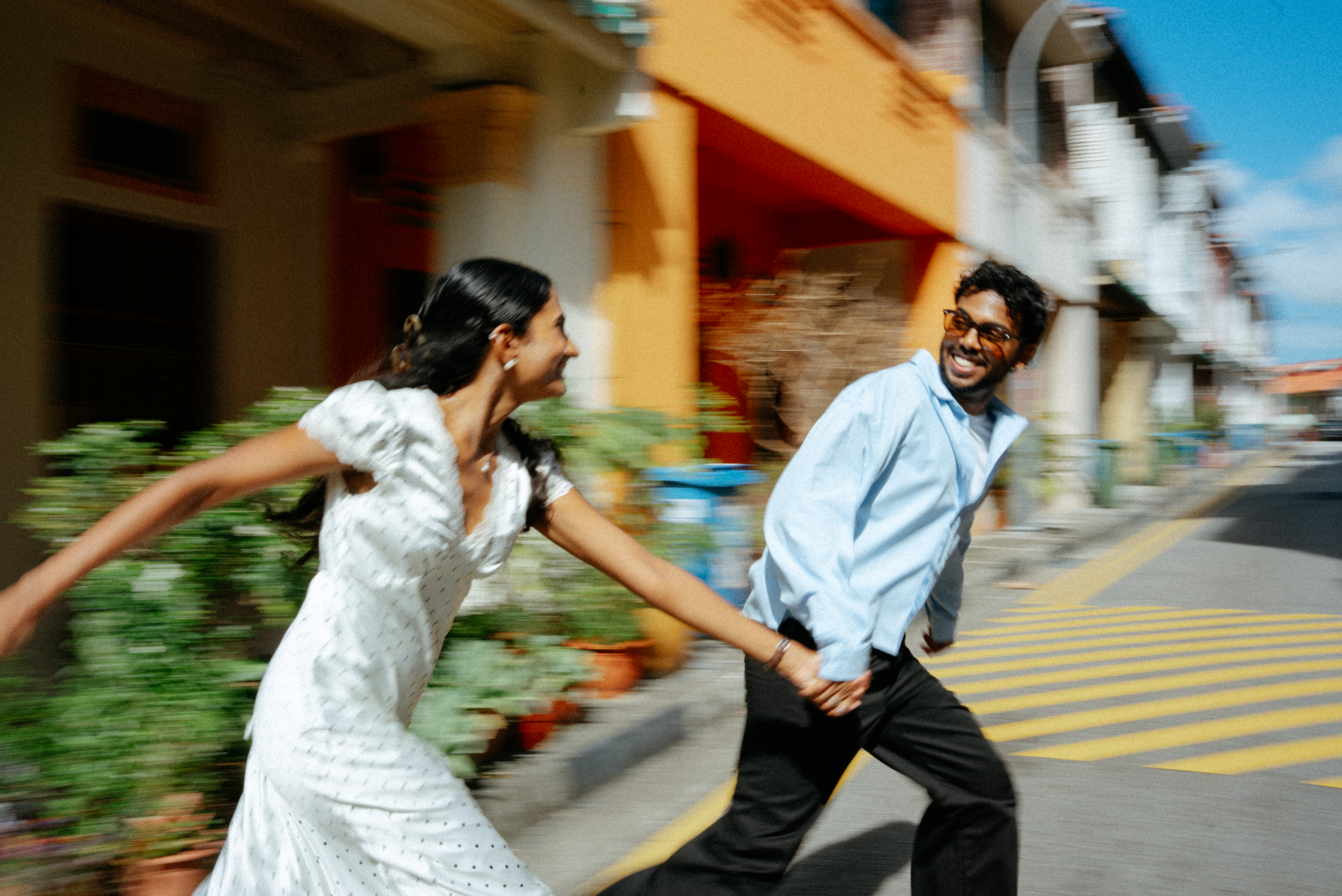 Janani and Dhanush running hand in hand through a colorful street
